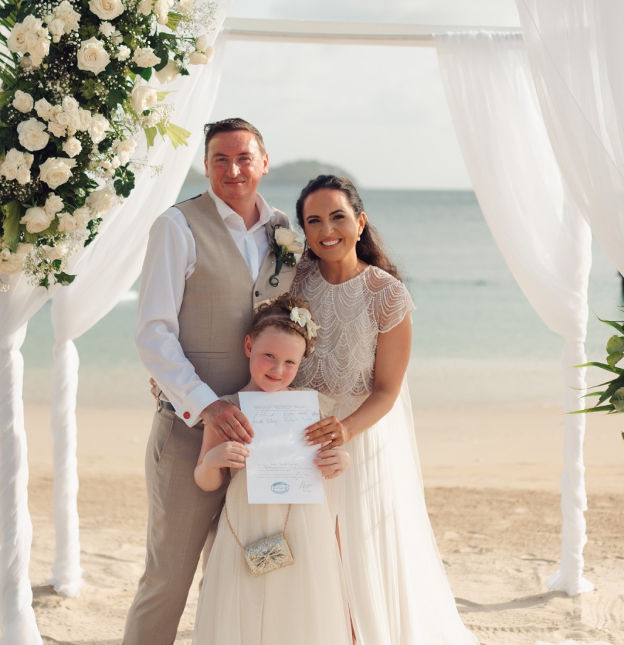 a man and woman holding a child under a white arch with flowers