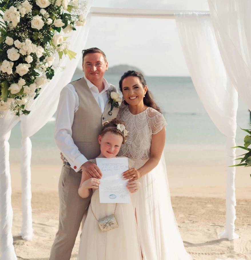 a man and woman holding a child under a white arch with flowers