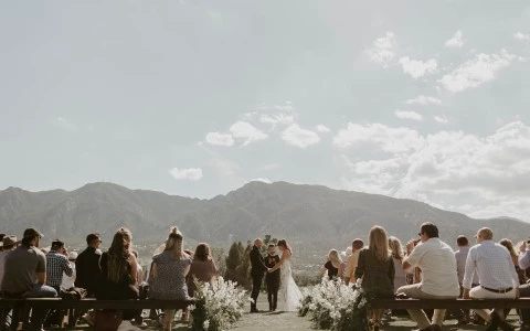 a bride and groom holding hands and standing on benches with people around them