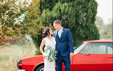 a man and woman in a wedding dress and suit standing next to a red car