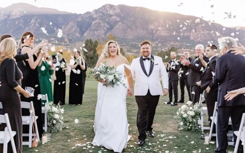 a bride and groom walking down a field with flower pedals being thrown