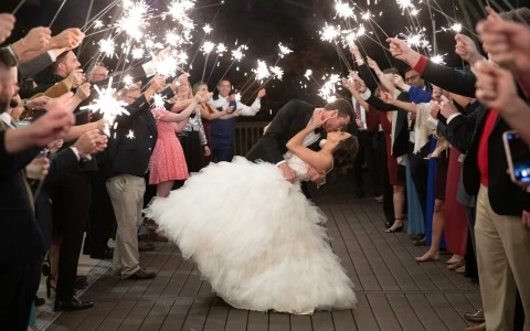 a man and woman kissing with guests holding sparklers