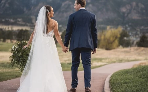 a man and woman holding hands and walking down a path