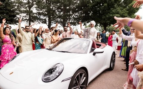 a man in a white suit riding in a convertible car with a crowd of people