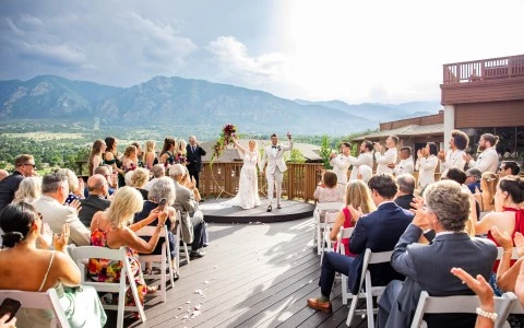 a couple in white wedding attire on a deck with a crowd of people