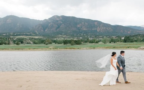 a man and woman in wedding attire walking alongside a lake