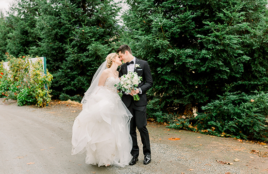 a man and woman kissing on a gravel path with trees